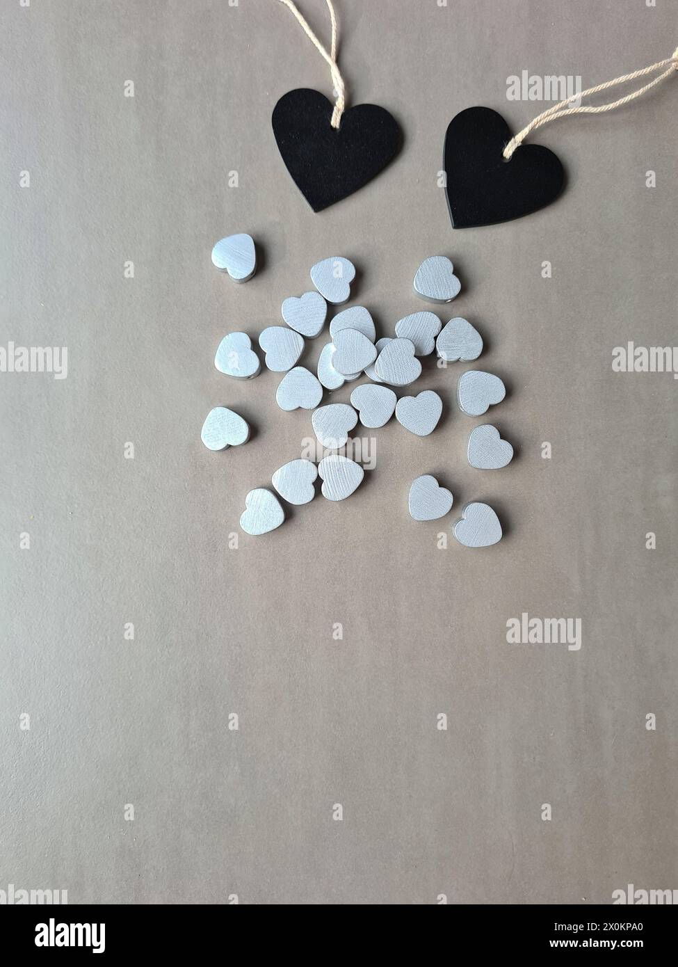 Zwei schwarze Holzherzen liegen neben vielen kleinen silberfarbenen Herzen Stockfoto