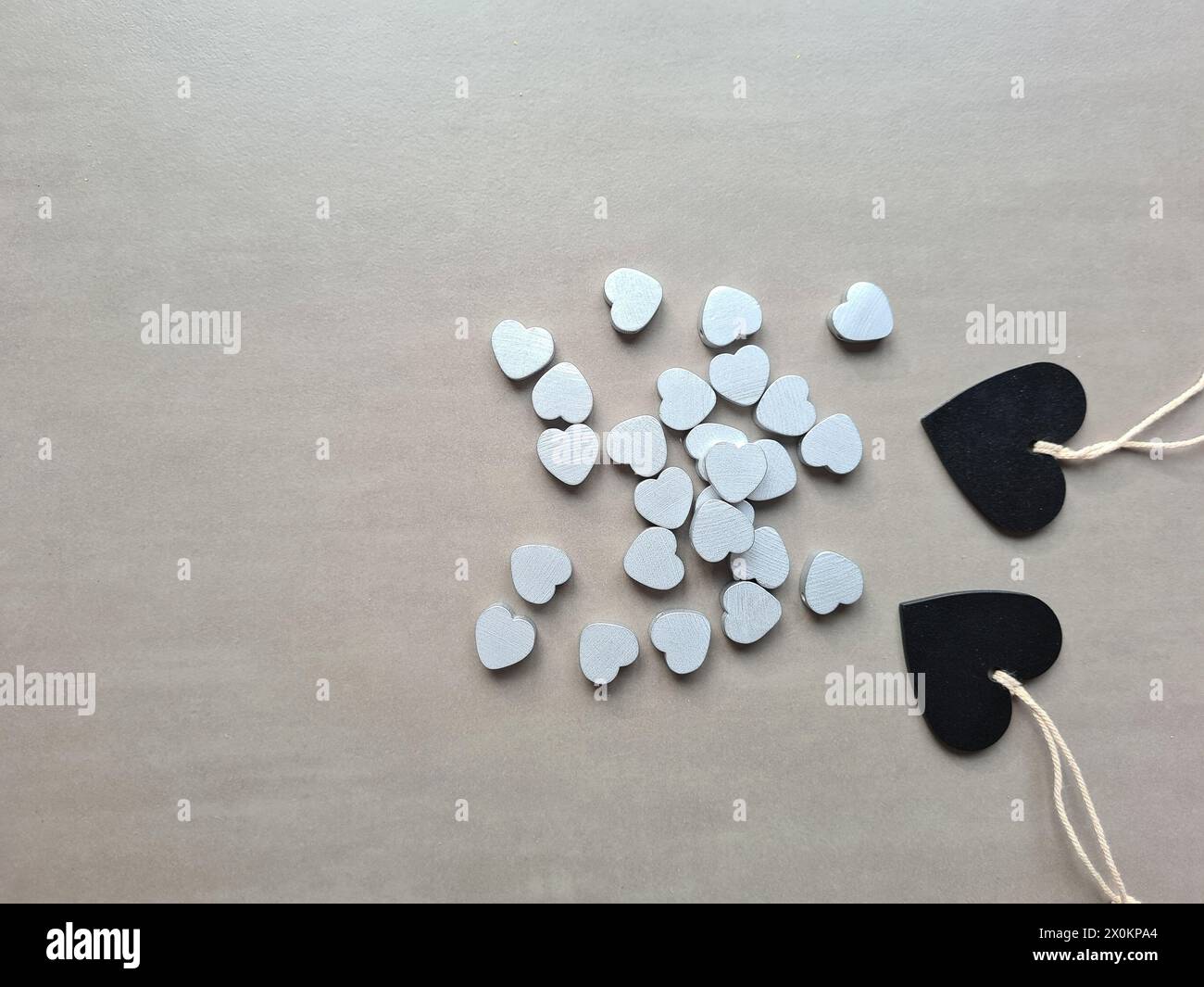Zwei schwarze Holzherzen liegen neben vielen kleinen silberfarbenen Herzen Stockfoto