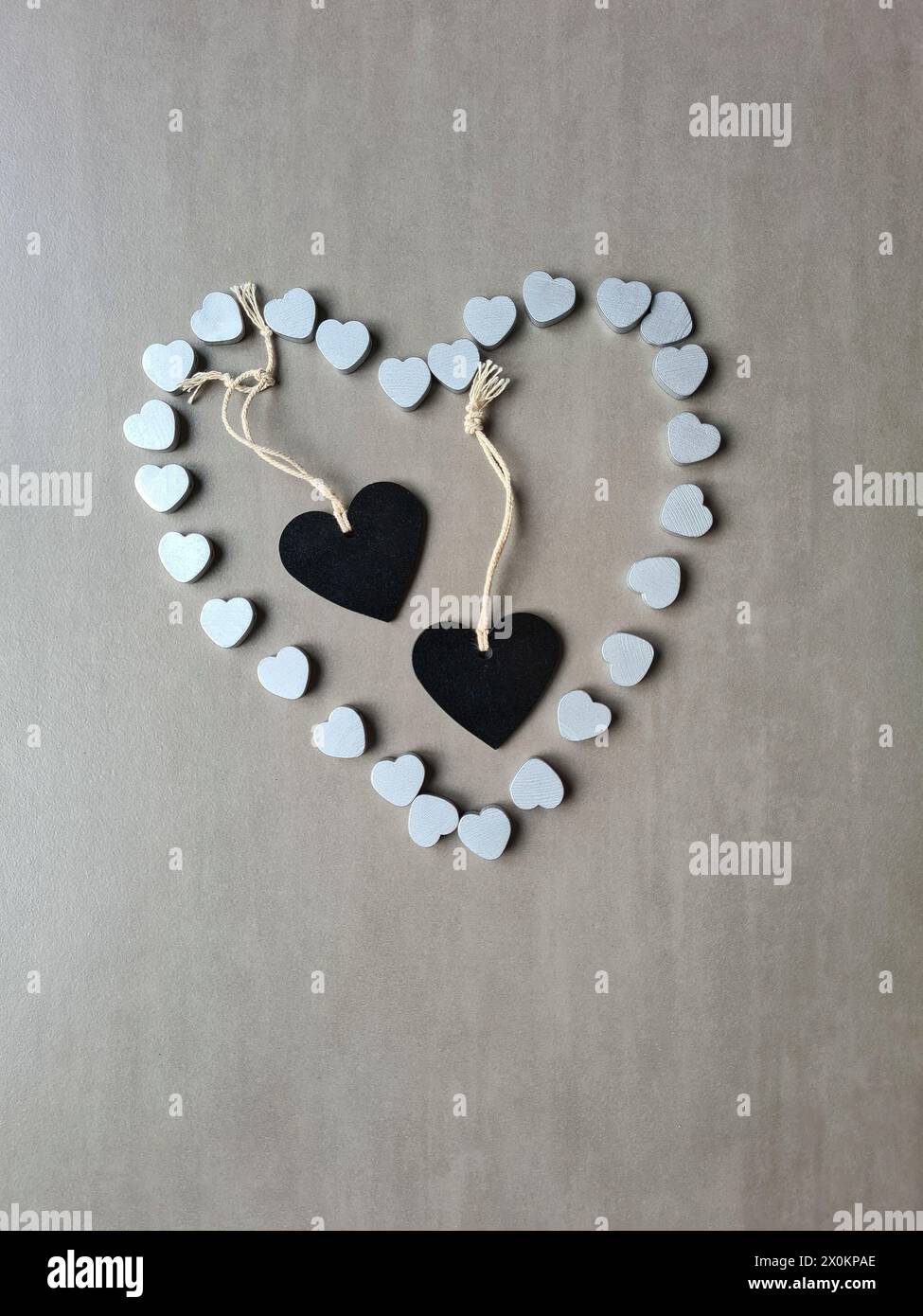 Zwei schwarze Herzen mit einem Band liegen in einer Herzform aus vielen kleinen silberfarbenen Herzen als Zeichen und Symbol der Liebe Stockfoto