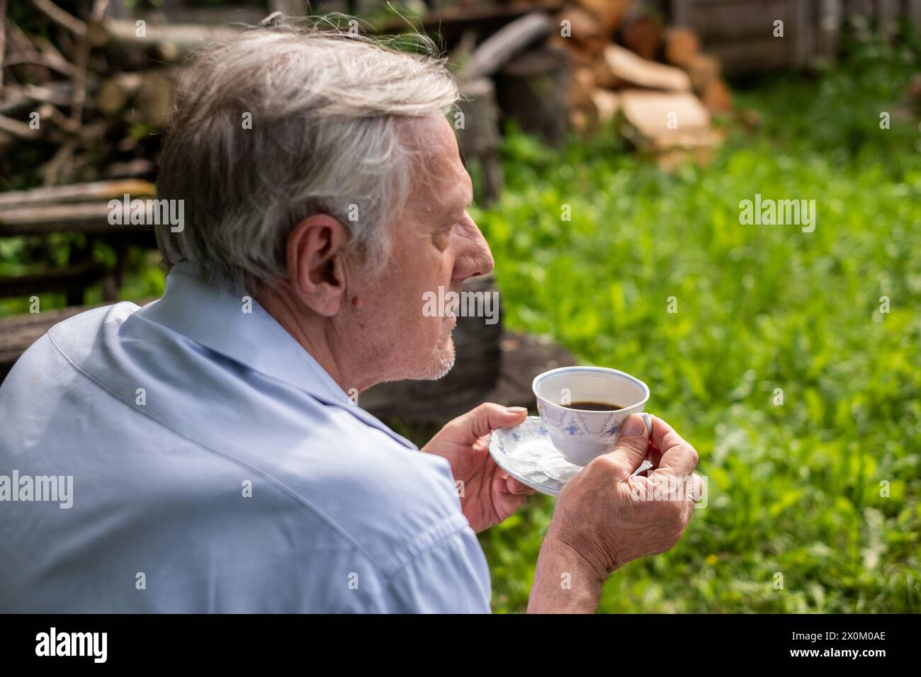 Mann im Profil hält eine Teetasse, blickt in die Ferne in einem üppigen Garten, ein Moment der ruhigen Reflexion und der Ruhe älterer Menschen. Hochwertige Fotos Stockfoto