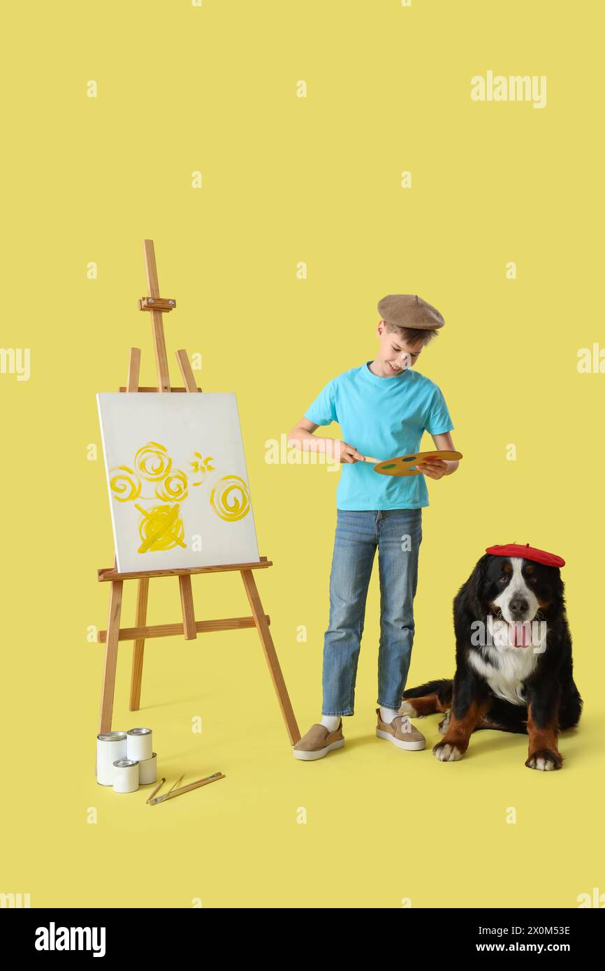 Kleiner Künstler mit Berner Berghund und Staffelei auf gelbem Hintergrund Stockfoto