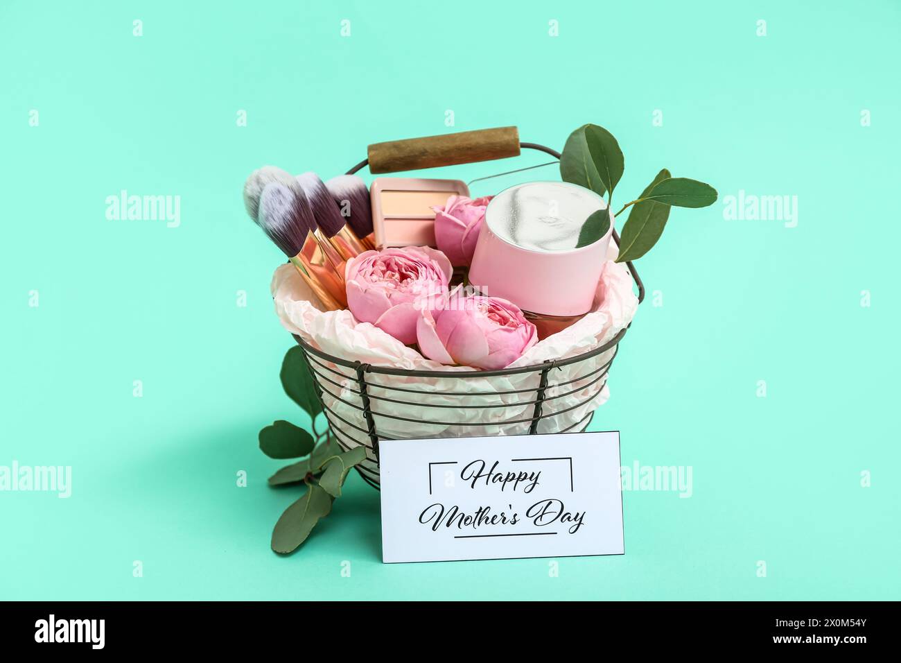Geschenkkorb mit Kosmetik, Make-up-Bürsten und Rosenblüten für Muttertagsfeier auf farbigem Hintergrund Stockfoto