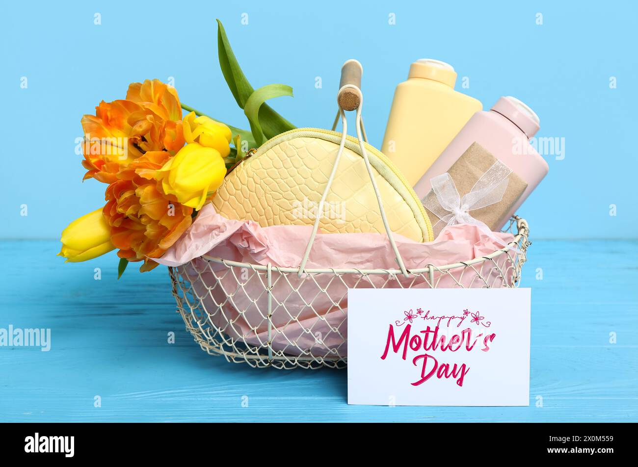 Geschenkkorb mit Kosmetikprodukten, schönen Tulpenblüten und Karte für Muttertagsfeiern auf farbigem Holztisch Stockfoto