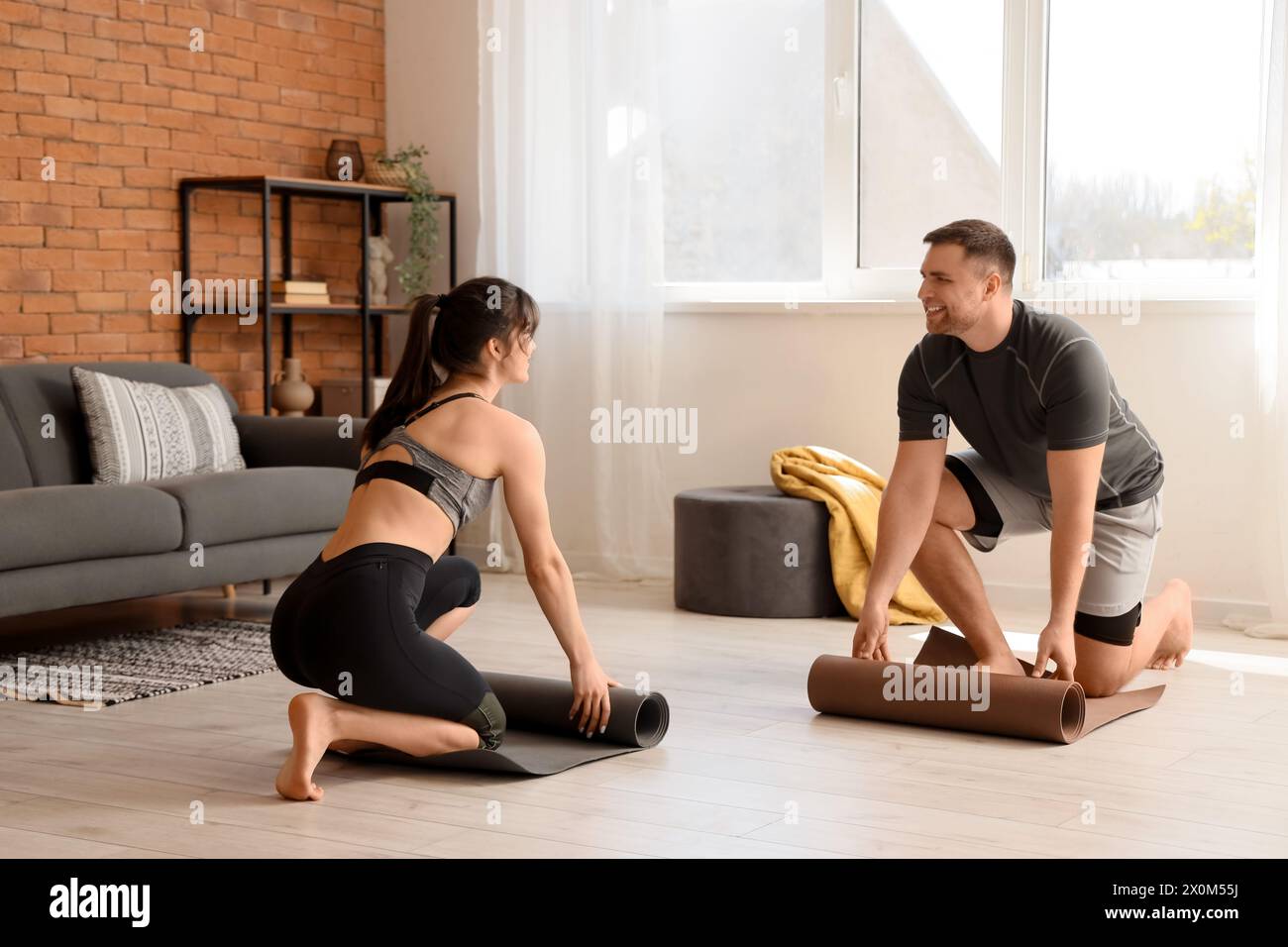 Sportliches junges Paar, das sich im modernen Wohnzimmer auf Yoga vorbereitet Stockfoto
