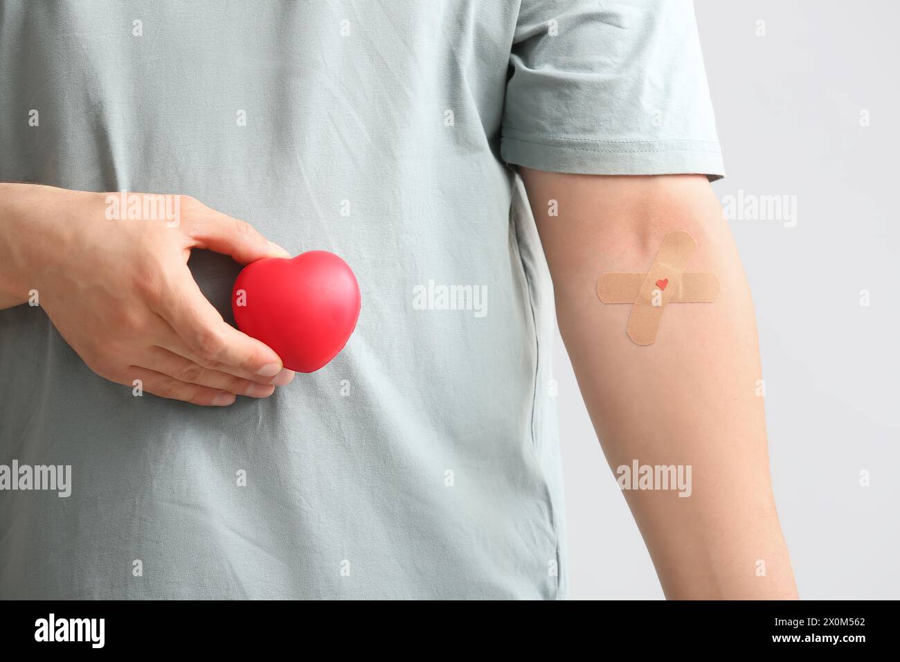 Blutspender mit appliziertem medizinischem Pflaster und Herz auf grauem Hintergrund, Nahaufnahme Stockfoto