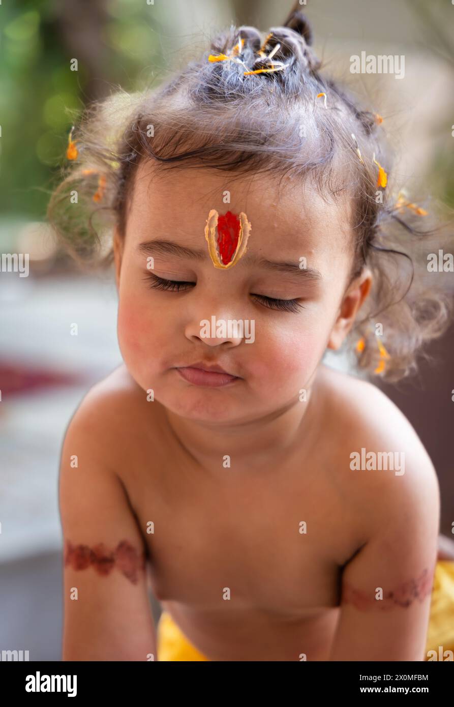 Niedliches indisches Jungen Auge geschlossen mit heiligem religiösem Symbol auf dem Kopf im Freien mit verschwommenem Hintergrund Stockfoto