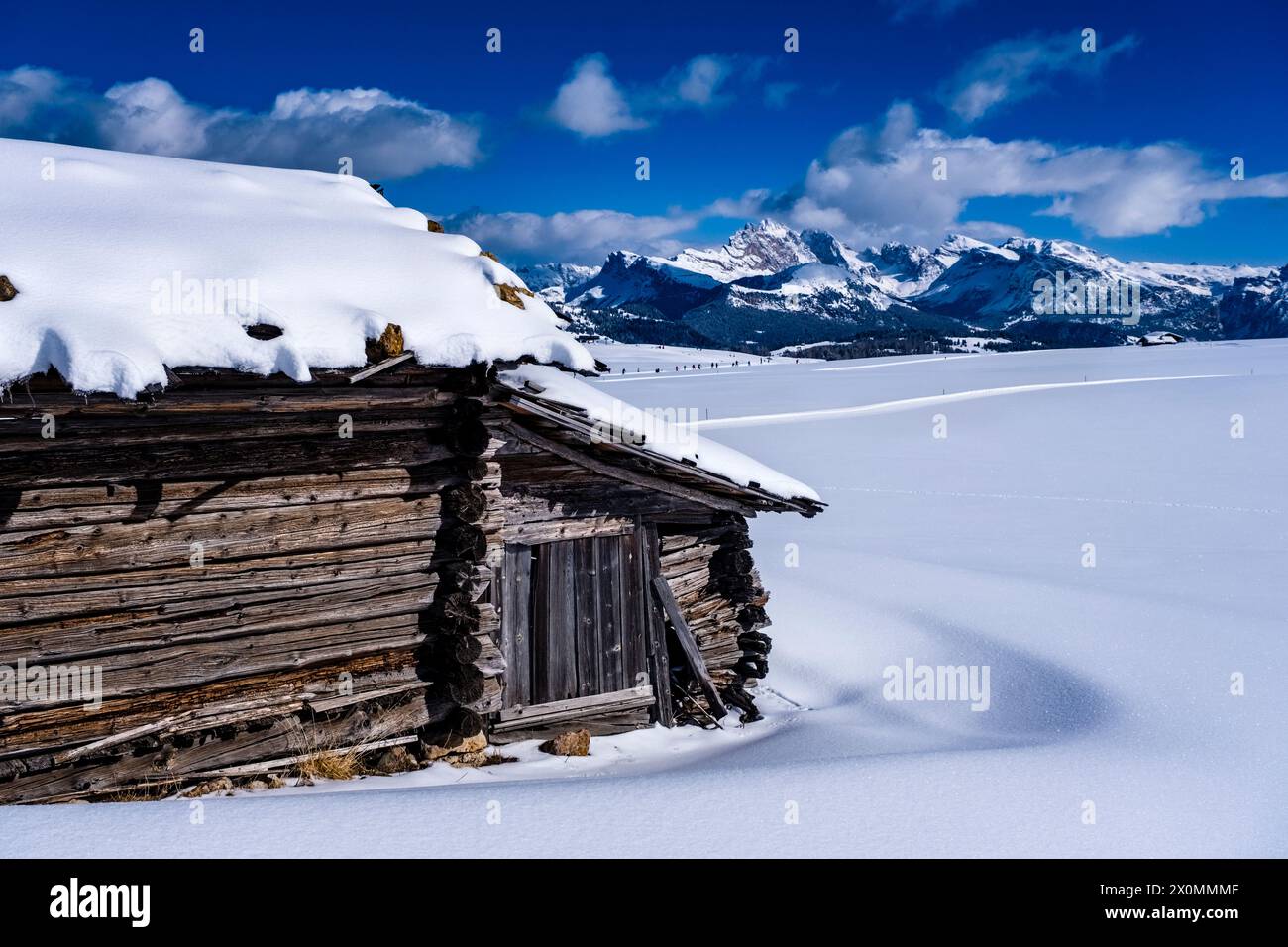 Hügeliges Ackerland mit schneebedeckten Weiden und einer Holzhütte auf der Seiser Alm im Winter, Gipfel der Geisgruppe in der Ferne. Stockfoto