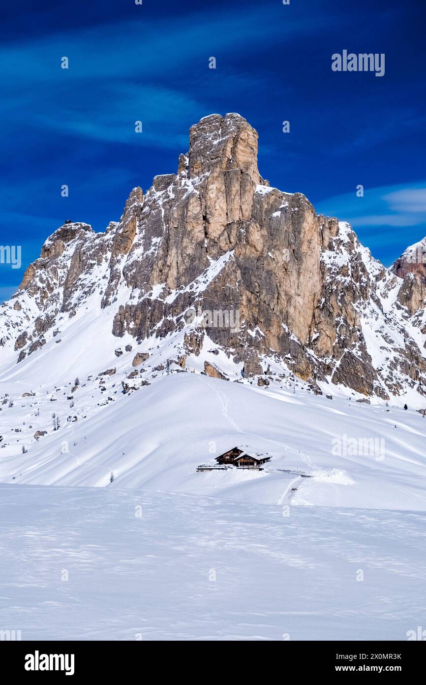 Schneebedeckte Hänge der alpinen Dolomitenlandschaft rund um den Giau Pass im Winter, den Gipfel des Ra Gusela und eine Almhütte in der Ferne. Stockfoto