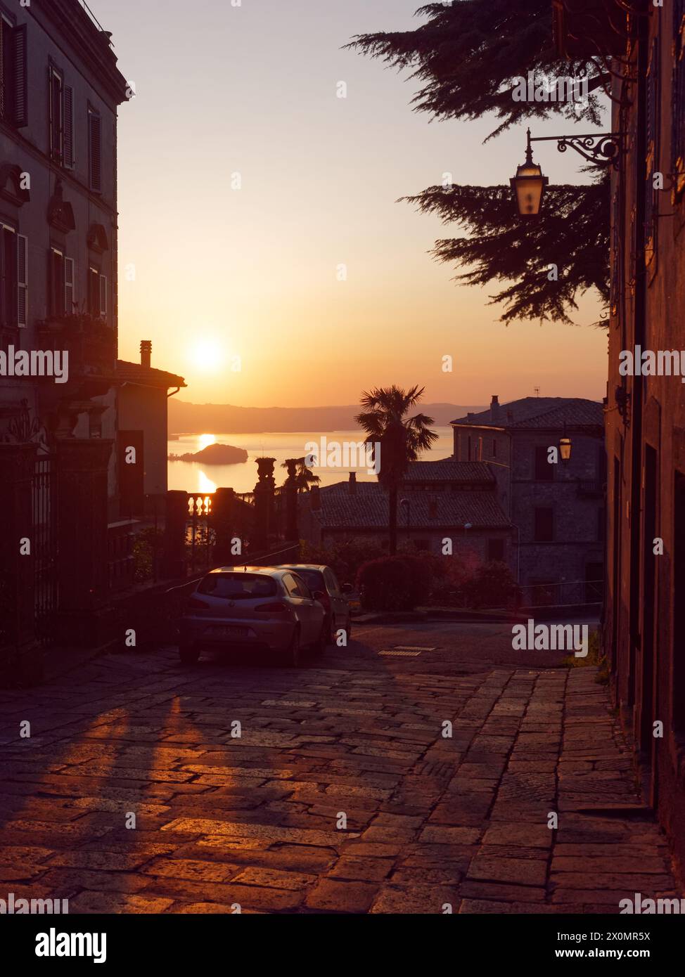 Malerische steile Straße bei Sonnenuntergang mit geparkten Autos mit Blick auf den Bolsena-See in Montefiascone, Provinz Viterbo, Region Latium, Italien. April 2024 Stockfoto