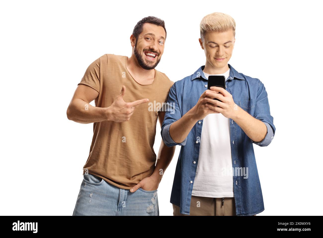 Junger Mann, der lacht und sich über einen Kerl lustig macht, der ein Smartphone auf weißem Hintergrund benutzt Stockfoto