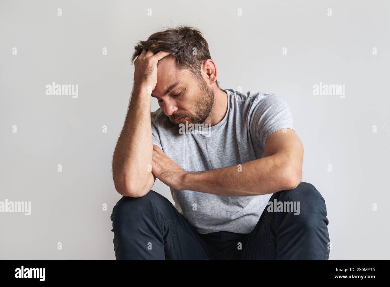 Das Konzept der männlichen psychischen Erkrankung. Der Mann sitzt auf dem Boden und lehnt seinen Kopf auf seine Hand. Stockfoto