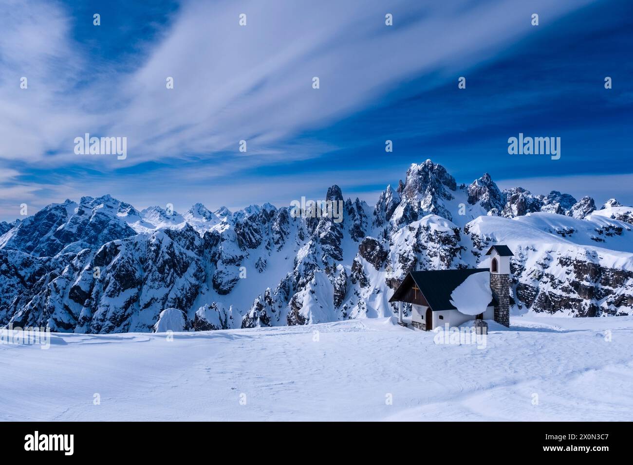 Die Kapelle Cappella degli Alpini im Naturpark Tre Cime im Winter, die alpine Dolomitenlandschaft und die Gipfel von Cadini di Misurina in der Ferne. Stockfoto