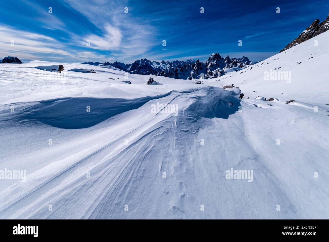 Schneeschwehungen schaffen kunstvolle Strukturen im Tre Cime Naturpark im Winter, die Gipfel von Cadini di Misurina in der Ferne, von der Forcella Lavared aus gesehen Stockfoto