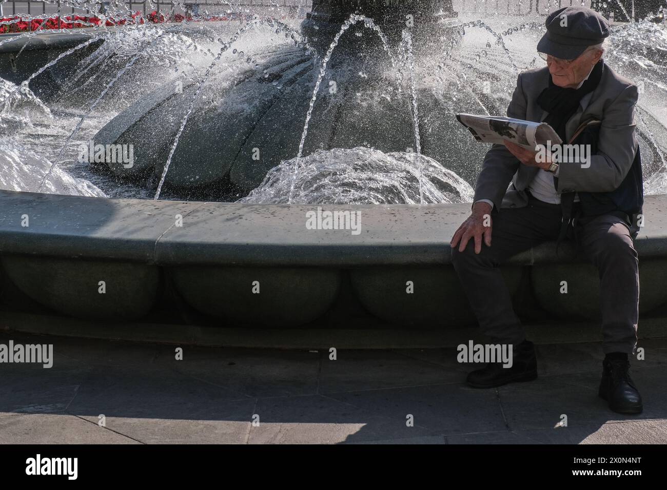 Jerusalem, Israel. April 2024. Ein älterer Mann liest eine Zeitung in der Nähe eines Springbrunnens am Pariser Platz, als Israelis am Rande wegen drohender iranischer Luftangriffe stehen. Quelle: Nir Alon/Alamy Live News Stockfoto