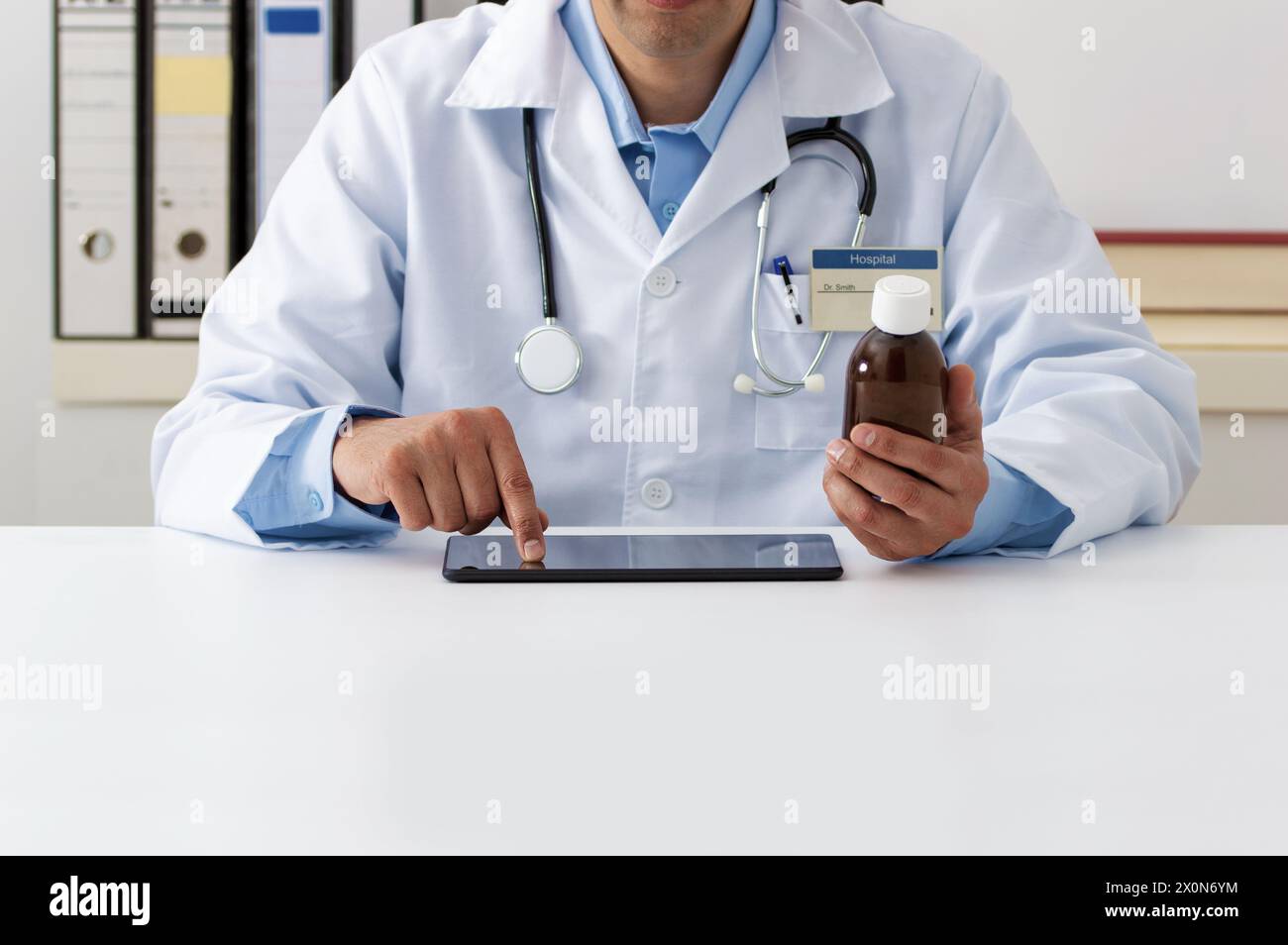 Foto eines jungen Arztes, der eine Tablette für ein Rezept in seiner Praxis mit einer Flasche antipyretischen Sirup in der Hand konsultiert Stockfoto