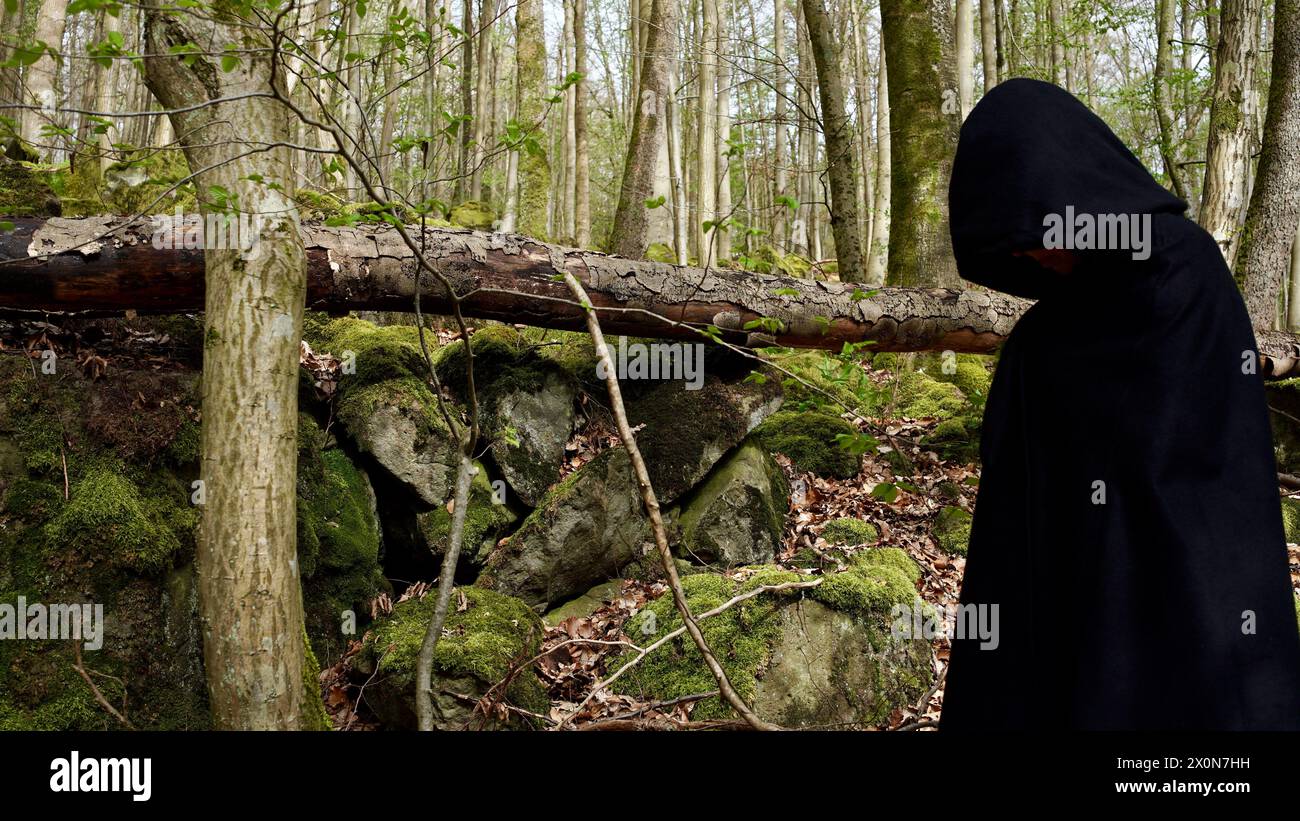 Eine gruselige Kapuzenfigur in einem schwarzen umhang im Wald. Stockfoto