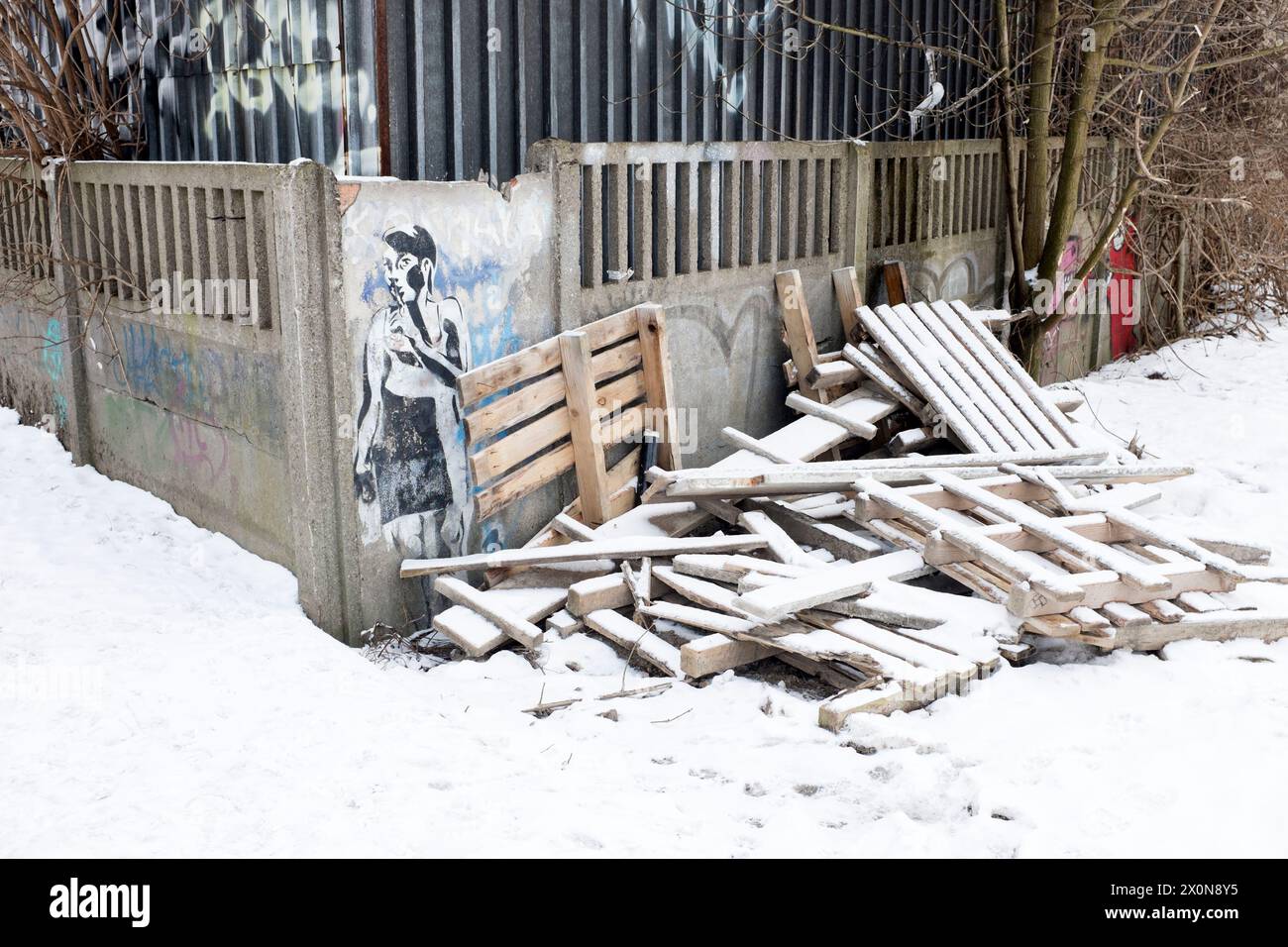 Street Art Graffiti eines Jungen mit Fingern auf den Lippen an einer Wand vor zerbrochenen Holzpaletten im Schnee in Krakau, Polen Stockfoto