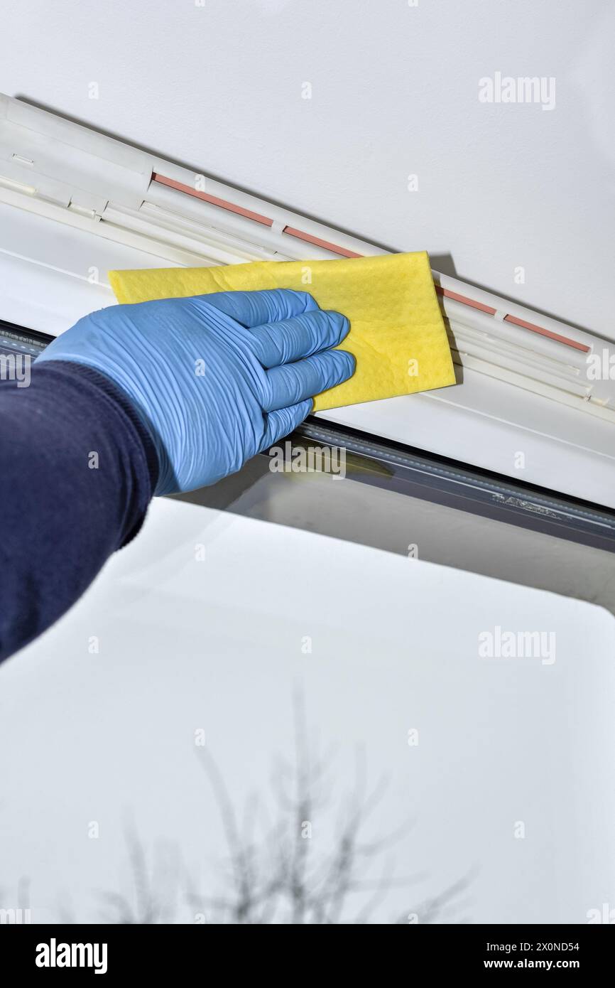 Reinigung des Lüftungsventils und des Kunststofffensters Eine Hand mit Handschuhen reinigt und wäscht den Rahmen eines Kunststofffensters mit einem Belüftungsventil von Staub und Di Stockfoto