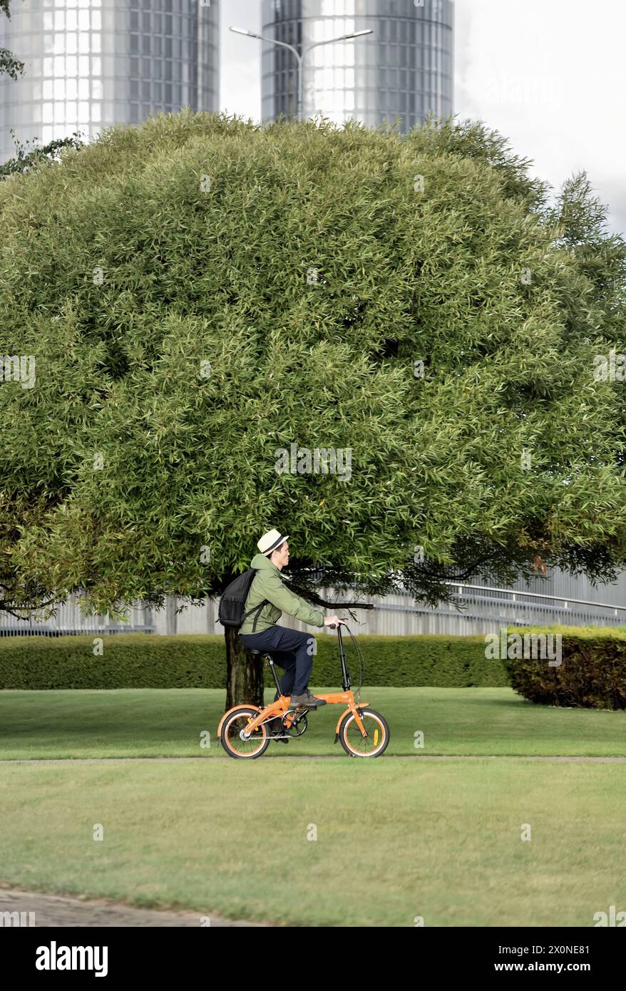Ein Mann fährt mit dem Fahrrad, um vor dem Hintergrund einer grünen Stadt zu arbeiten. Fahrrad umweltfreundlicher Transport in der Stadt. Stockfoto