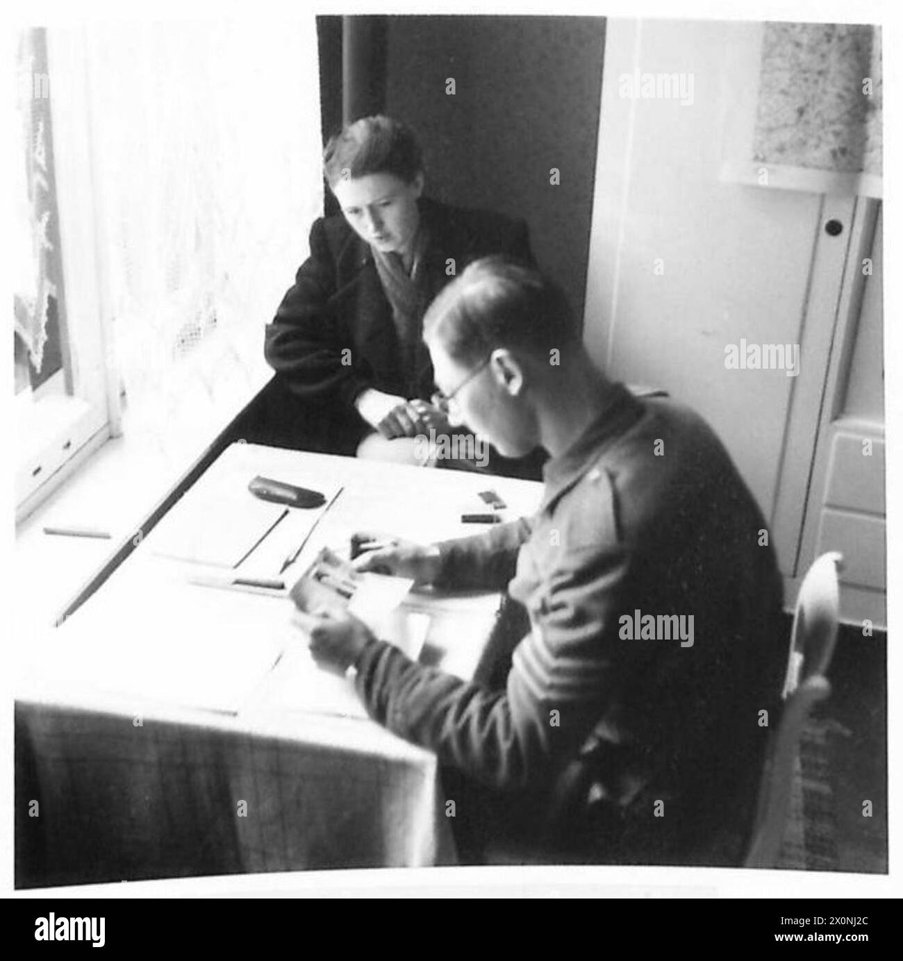 SICHERHEITSLEUTE AM ARBEITSPLATZ - Ursula Pries, die auch Schreibkraft im Gestapo-Büro Lubecks war, wurde von einem F.S.I.-Sergeant verhört. Fotografisches negativ, britische Armee, 21. Armeegruppe Stockfoto