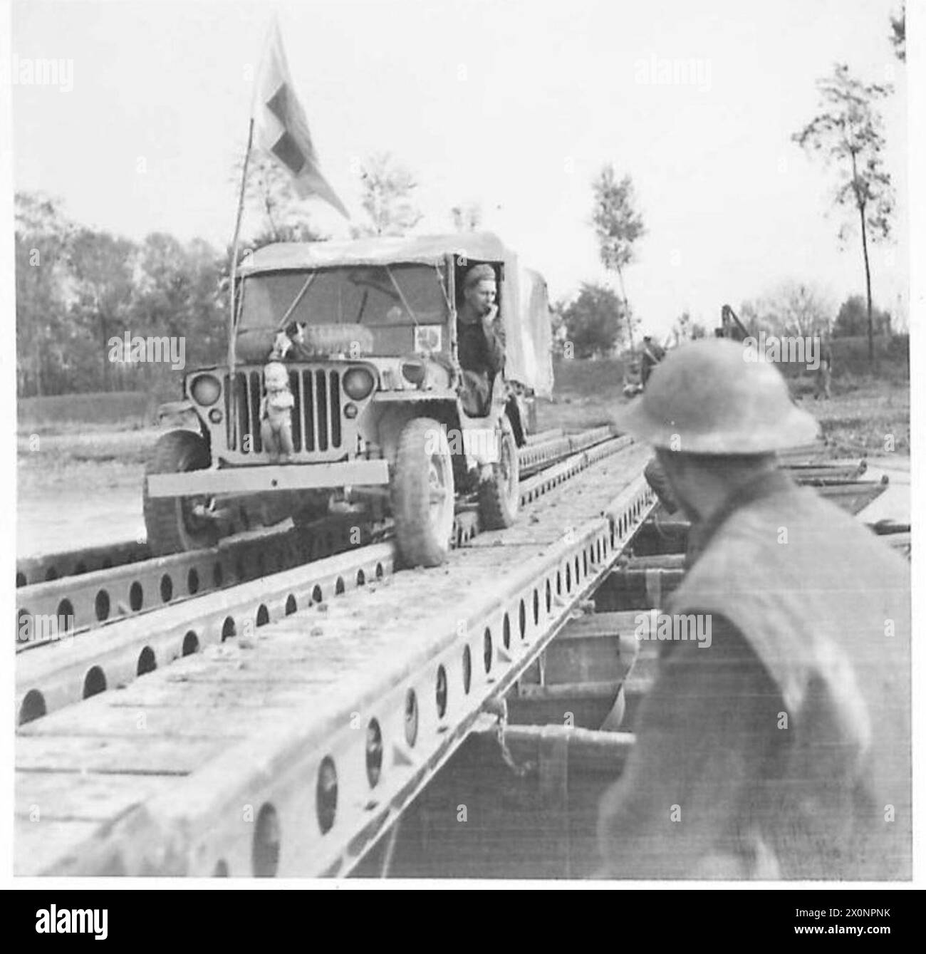 Ein Polizist schickt ein Pfadfinderauto auf die Landebahn der Brücke während der Überquerung des Flusses Ronco. Fotografisches negativ, britische Armee. Stockfoto