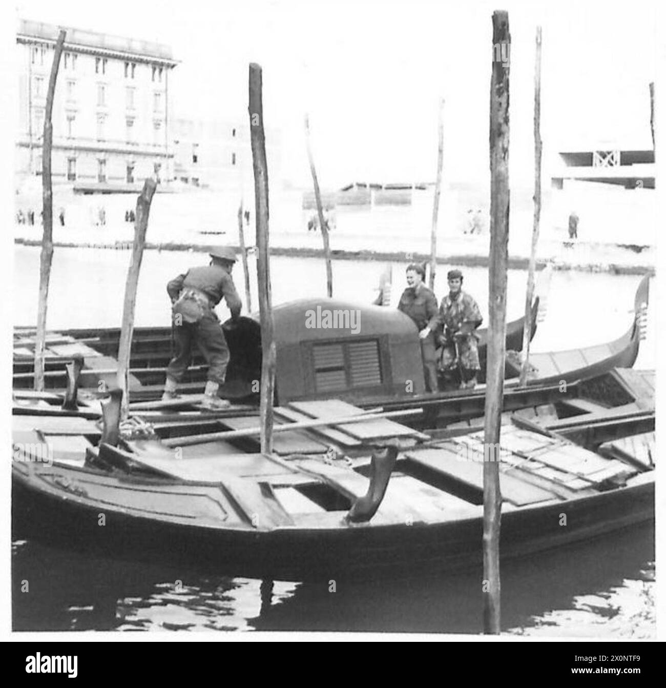 Ein Partisanen führt die britischen Truppen der achten Armee über eine venezianische Gondel und dokumentiert die Truppenbewegung und die lokale Zusammenarbeit während des Vormarsches nach Venedig. Fotografisches negativ der britischen Armee. Stockfoto