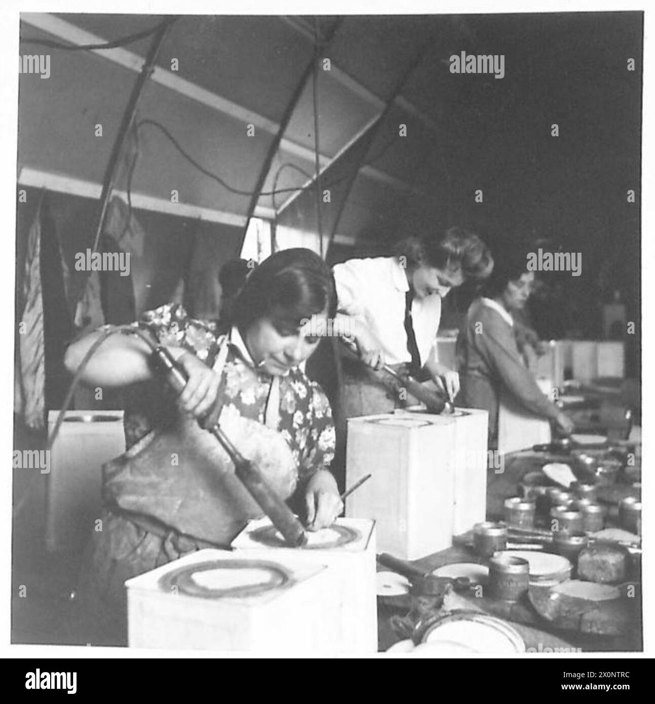 Fotografisches negativ, das das Personal der britischen Armee zeigt, das Dosen in einem Versorgungsreserve-Depot lötet und versiegelt, was militärische Vorräte und Lageroperationen veranschaulicht. Stockfoto Fotografisches negativ, das das Personal der britischen Armee zeigt, das Dosen in einem Versorgungsreserve-Depot lötet und versiegelt, was militärische Vorräte und Lageroperationen veranschaulicht. Stockfoto