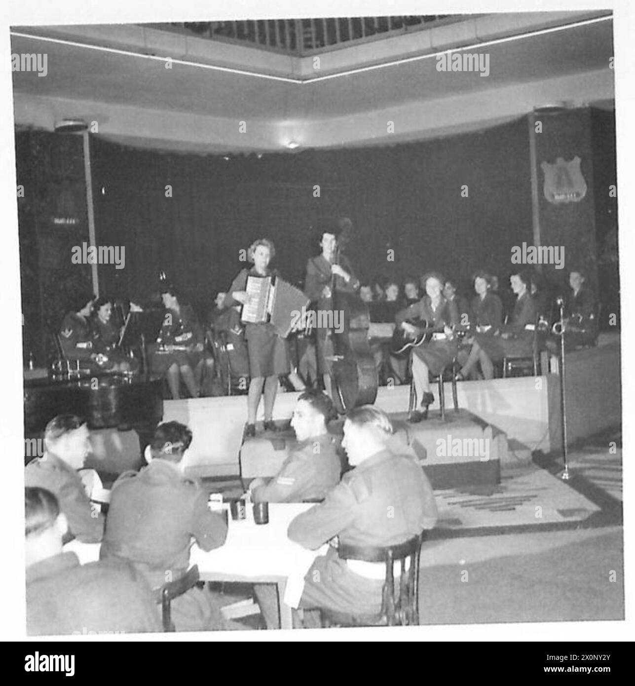 Ein Musiktrio tritt mit Akkordeon und Streichinstrumenten auf, während der Rest der britischen Armee während einer Aufführung im Hintergrund zu sehen ist. Stockfoto