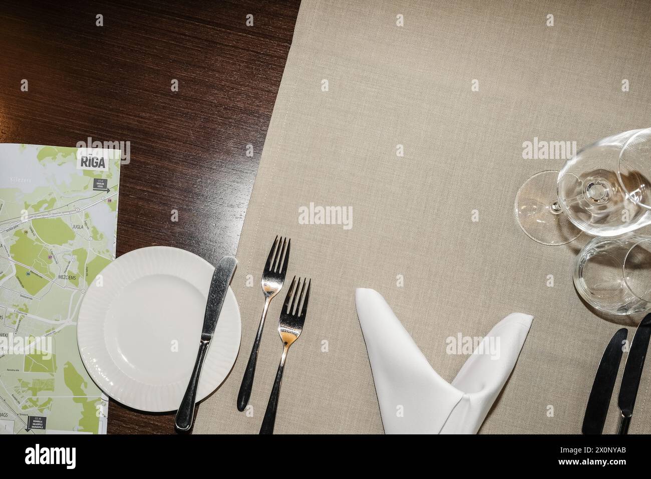 Blick von oben auf einen servierten Tisch in einem Restaurant mit Geschirr und Gläsern für Speisen und Getränke und eine Karte von Riga, Lettland für einen Reisenden. Stockfoto