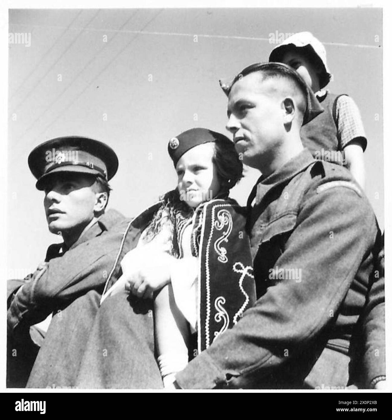 Ein griechisches Kind in Nationalkleidung ist mit zwei britischen Soldaten während des Besuchs des griechischen Königs bei seinen Truppen zu den Feierlichkeiten zum Nationalfeiertag abgebildet. Stockfoto Ein griechisches Kind in Nationalkleidung ist mit zwei britischen Soldaten während des Besuchs des griechischen Königs bei seinen Truppen zu den Feierlichkeiten zum Nationalfeiertag abgebildet. Stockfoto