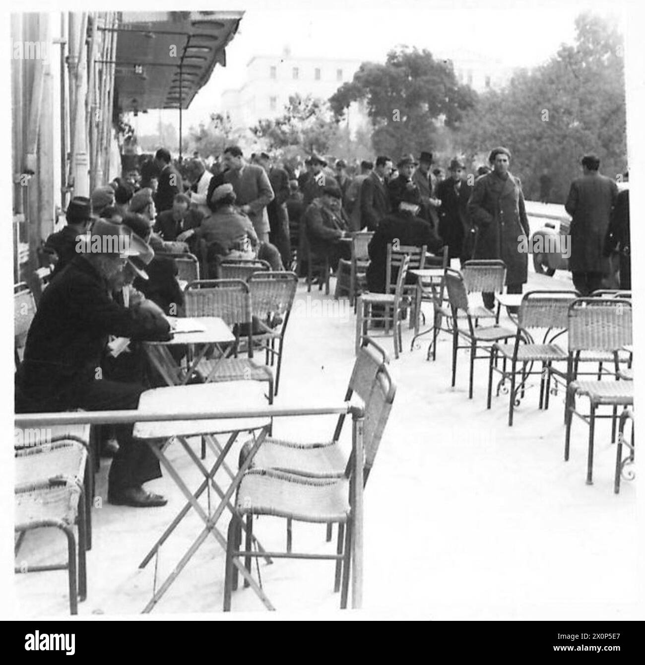 Griechische Zivilisten nehmen die traditionellen Bräuche in Athen wieder auf, trinken Kaffee vor Geschäften und beobachten das Straßenleben, fotografiert von der britischen Armee. Stockfoto