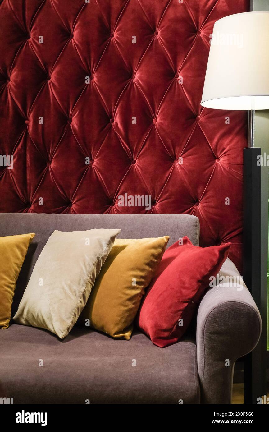 Sofa oder Couch mit verschiedenen Farben, Kissen gegen rote gepolsterte Wand in klassischem Innendesign, Wohnzimmer zum Ausruhen und Lounge Stockfoto