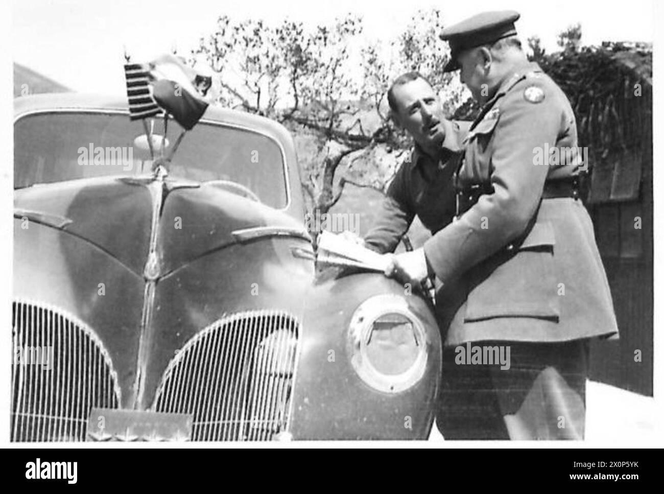 Die Generäle Wilson und Leese diskutieren die Schlachtpläne mit Karten auf der Motorhaube des C-in-C-Autos, die britische, amerikanische und polnische Flaggen zeigen, während eines Besuchs der 8. Armee in Italien. Stockfoto