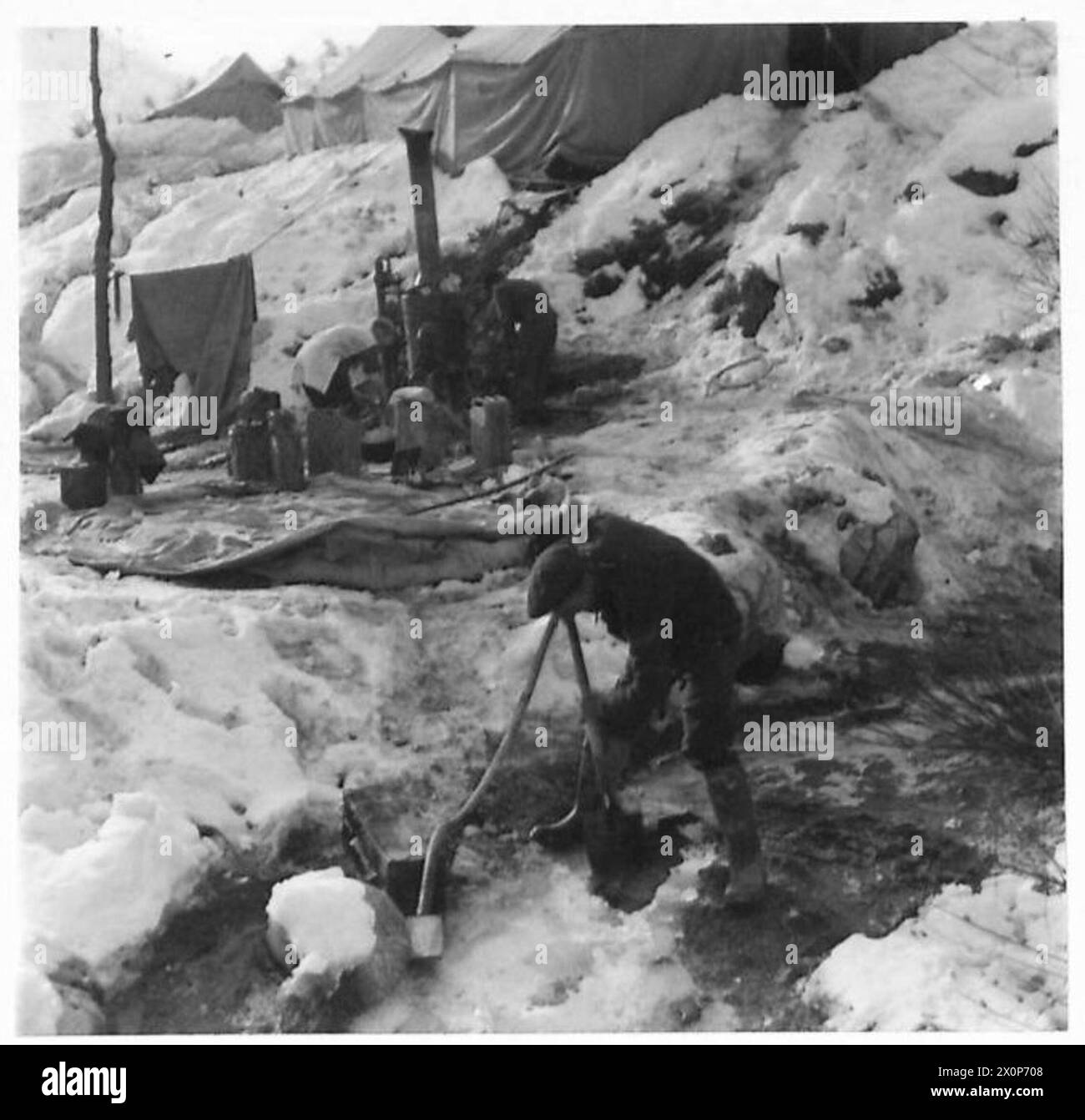 CPL. T. Doran bereitet ein Loch in einem eisbedeckten Fluss vor, um den britischen Truppen Wasser für heiße Duschen zu liefern, mit Kesseleinheit und Badzelt im Hintergrund. Stockfoto