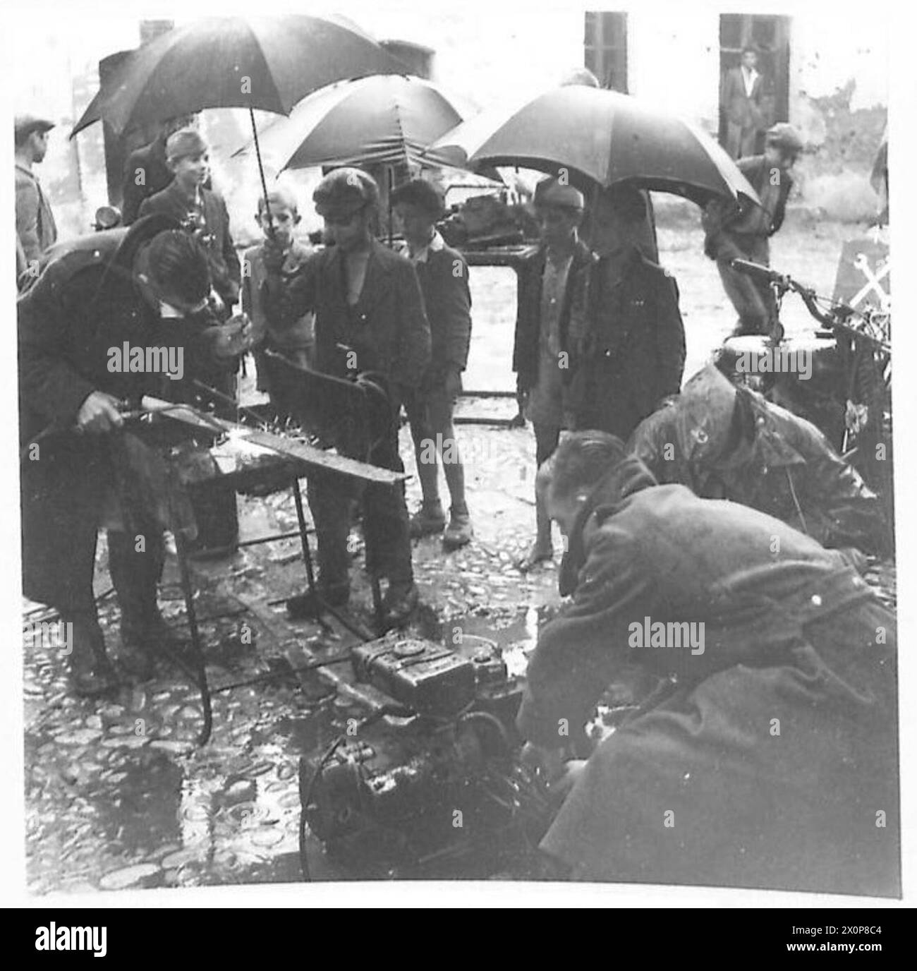 WÄHREND DIE ACHTE ARMEE IN ITALIEN IN SINTFLUTARTIGEN REGENFÄLLEN VORRÜCKT, werden die Männer, die die Räder der 8. Armee drehen, hier gesehen, wie sie wie üblich auf einem Dorfplatz, umgeben von einem unvermeidlichen Sichter, weitermachen. wer, solange er einen Schirm hatte, bleibt nicht drinnen. Fotografisches negativ, britische Armee Stockfoto