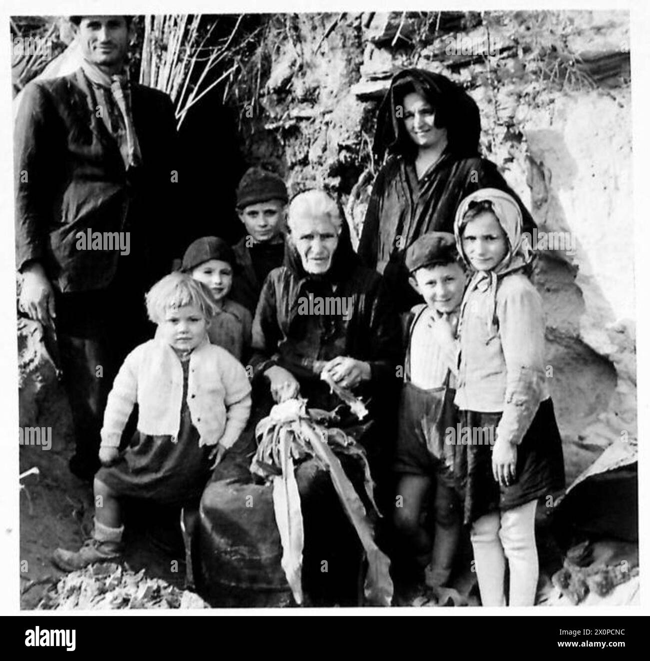 Eine Gruppe italienischer Zivilisten ist am Eingang einer Grottenunterkunft in einem Dorf an der Front der 8. Armee in Italien während des Zweiten Weltkriegs abgebildet. Das Foto dokumentiert die Anwesenheit von Zivilisten in der Nähe militärischer Stellungen. Stockfoto