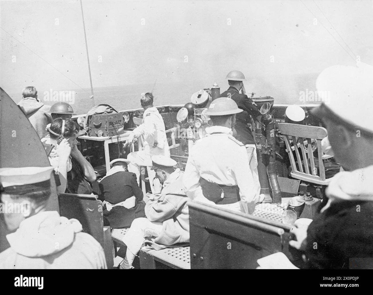 DIE NAVY IST TEIL DES VORMARSCHES IN ITALIEN. 12. MAI 1944 AN BORD DES KREUZERS HMS DIDO IM MITTELMEER. DIE DIDO FÜHRTEN MIT EINER ESKORTE AMERIKANISCHER ZERSTÖRER SCHIKANIERENDES FEUER AUF DEM APPIAN WAY IN DER GEGEND VON TERRACINA UND AUF FEINDLICHE SCHWERE ARTILLERIE, DIE SICH DER FÜNFTEN ARMEE IN DER GEGEND VON GAETA WIDERSETZTE. KAPPE auf der Brücke des Kreuzers DIDO während des Bombardements leitet der Geschützoffizier Lieut A Cavendish, RN (im Duffle Coat) das Feuer. Der Signaloffizier (mittlerer Hintergrund) erhält Berichte von dem beobachtenden Flugzeug. Admiral John M Mansfield, DSC, befindet sich auf der rechten Seite, zurück zur Kamera, in t Stockfoto