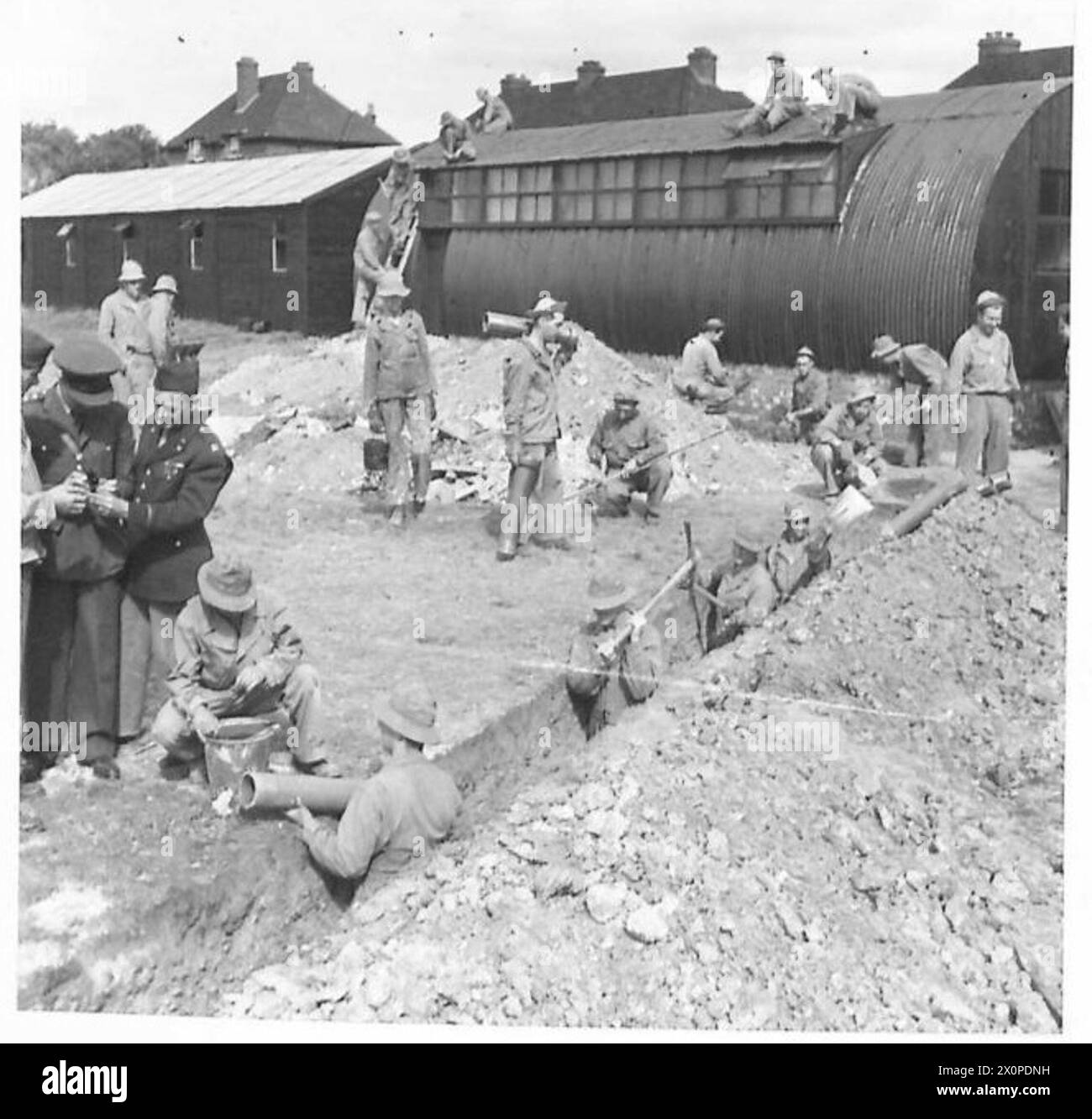 AMERIKANISCHE TRUPPEN HELFEN – britische und US-Offiziere beobachten ein Rohrverlegungsteam bei der Arbeit auf dem Gelände. Fotografisches negativ, britische Armee Stockfoto