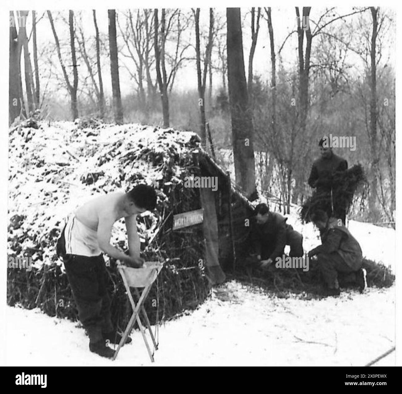 Die Truppen bauen eine Hütte aus verfügbaren Materialien, während ein Soldat während einer Kampfpatrouille in eiskaltem Wasser wäscht. Fotografisches negativ, britische Armee. Stockfoto