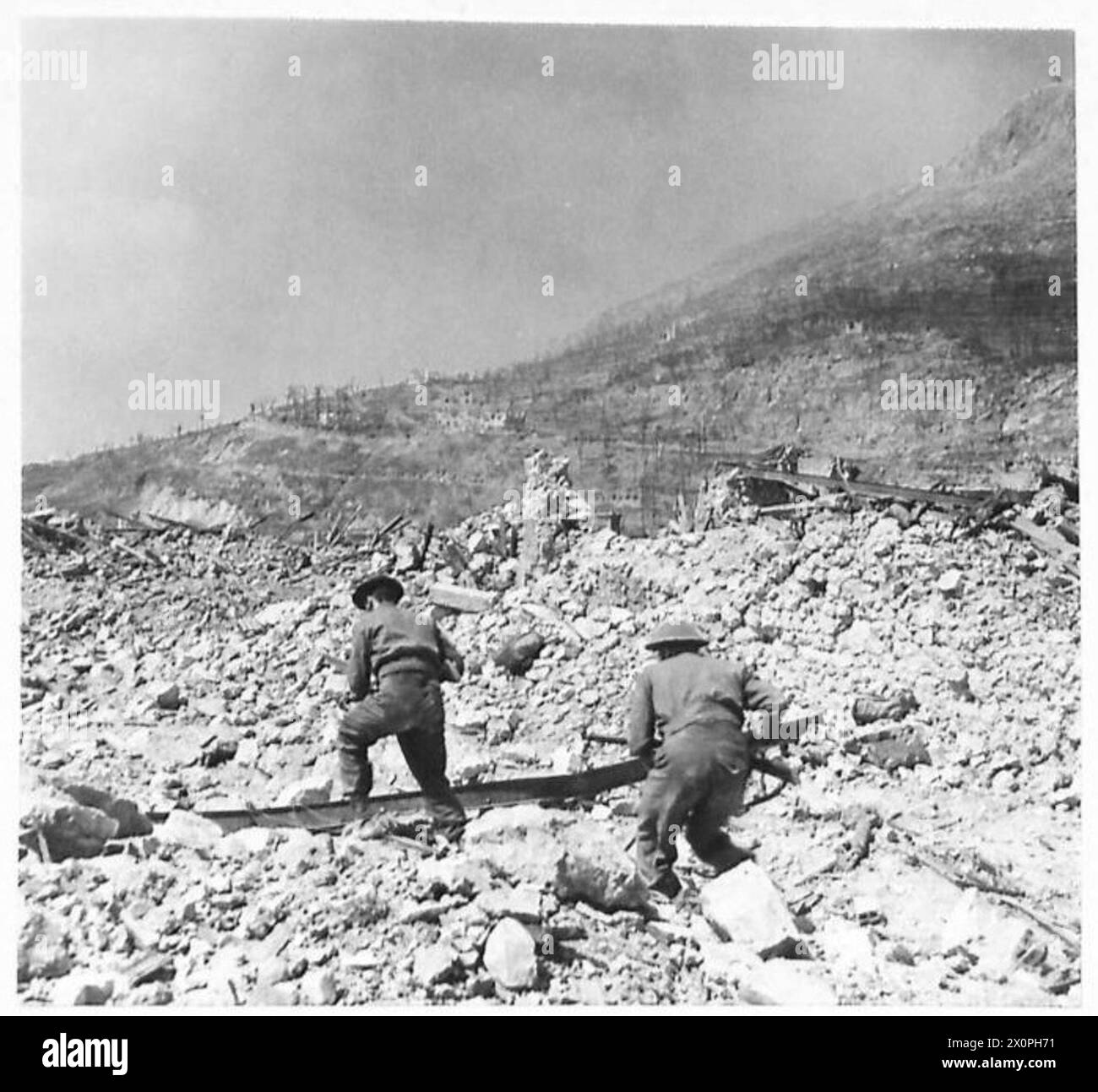 Zwei britische Soldaten dringen durch die Ruinen von Cassino vor, um einen deutschen Scharfschützen während des Italienischen Feldzugs zu neutralisieren. Das Bild dokumentiert Kampfaktivitäten in einem zerstörten Stadtgebiet. Stockfoto