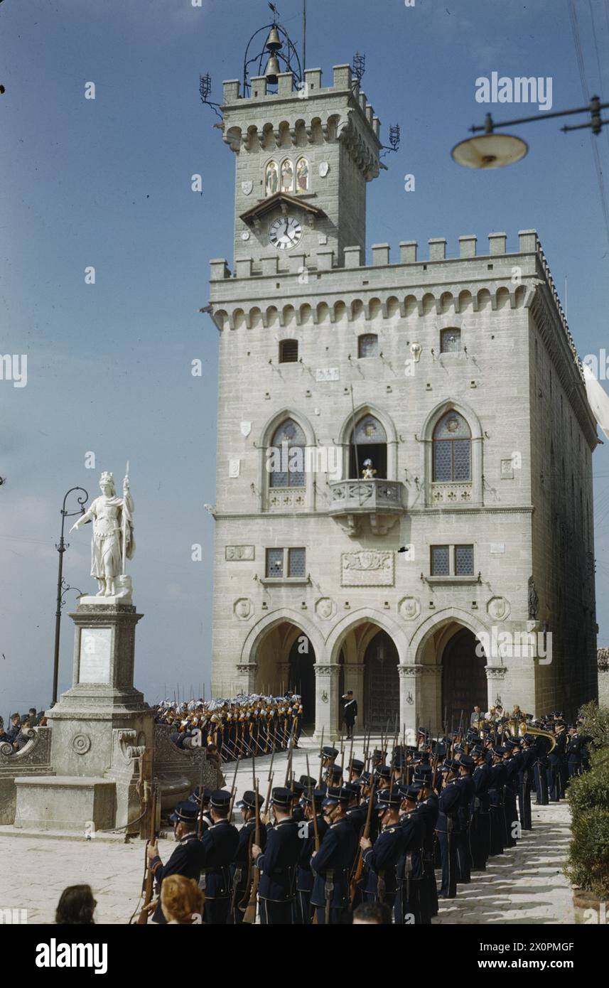 DIE EINWEIHUNG NEUER REGENTEN FÜR SAN MARINO, ITALIEN, 1. OKTOBER 1944 - Truppen präsentieren während des Spiels der Nationalhymne auf dem Hauptplatz von San Marino Waffen, während die Flagge der Republik San Marino auf dem Balkon des Regentenpalastes aufgerollt wird. Bei der Zeremonie wurden zwei Regenten eingeweiht, um sechs Monate lang zu regieren Stockfoto