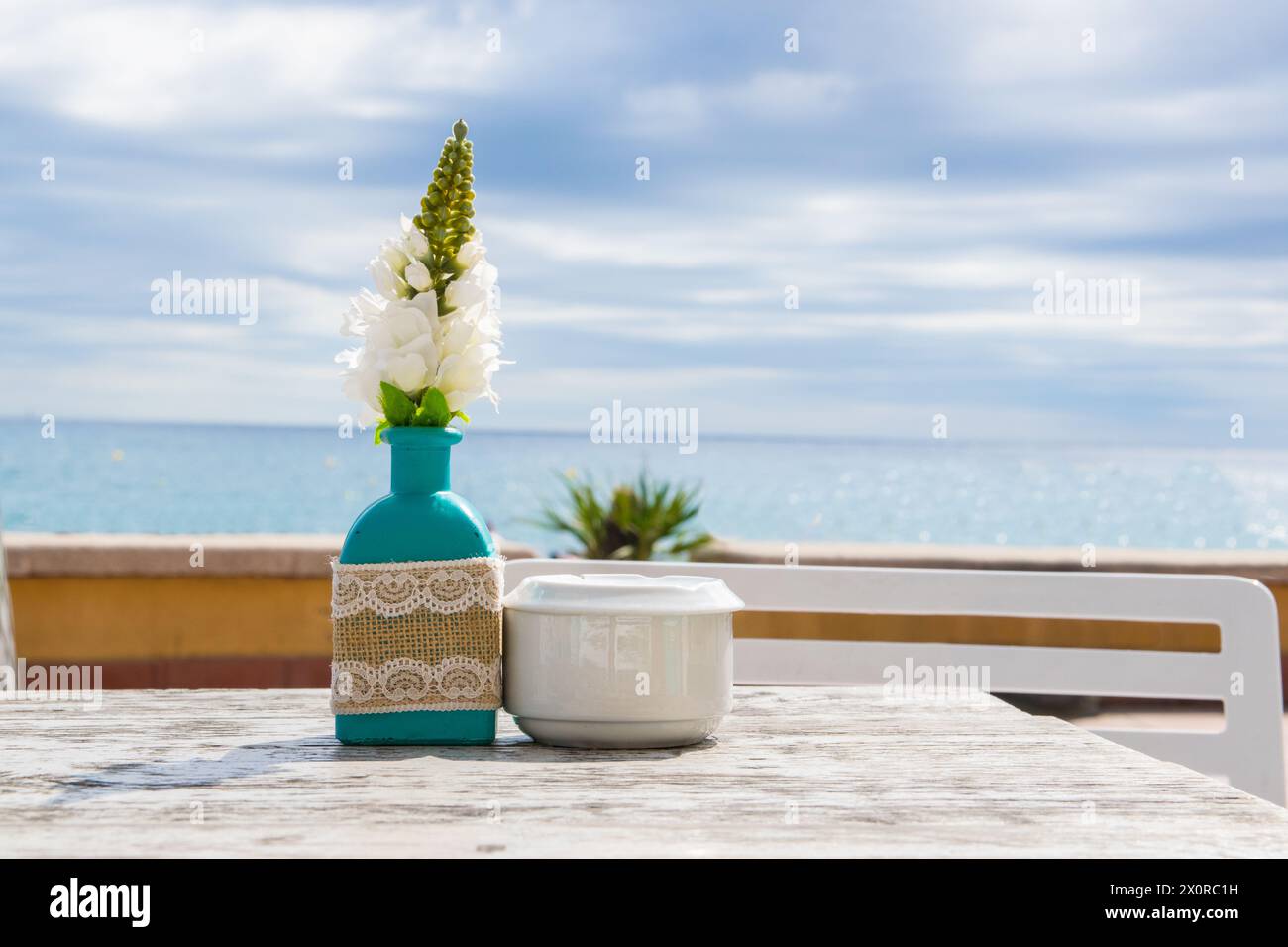 Lagerhaus im Freien. Stühle und Tische draußen bei Sommersonnenwetter. Vase mit Blumen auf dem Tisch für ein Sommercafé mit Meerblick. Stockfoto