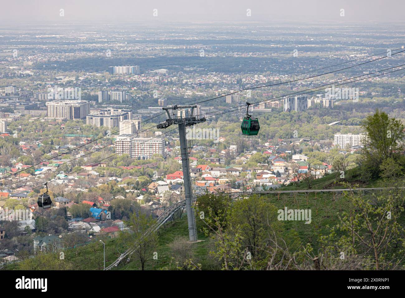 Seilbahn mit zwei Kabinen, vor dem Hintergrund der Stadt im Frühling. Mit dem Flugzeug zum Kok Tobe Hügel in Almaty, Kasachstan. Touristenort, City la Stockfoto