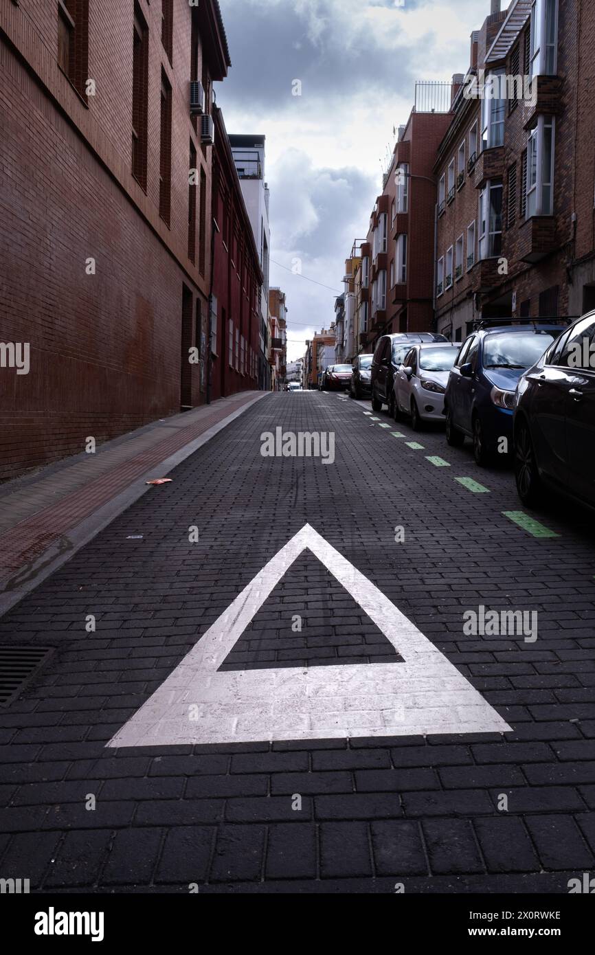 Urbane Szene. Ein „Ertrag“-Schild hebt sich vor dem schwarzen Asphaltgrund der Stadt ab, geparkte Autos, urbane Mobilität, Respekt, Verkehr, und Sonnenaufgang im Th Stockfoto