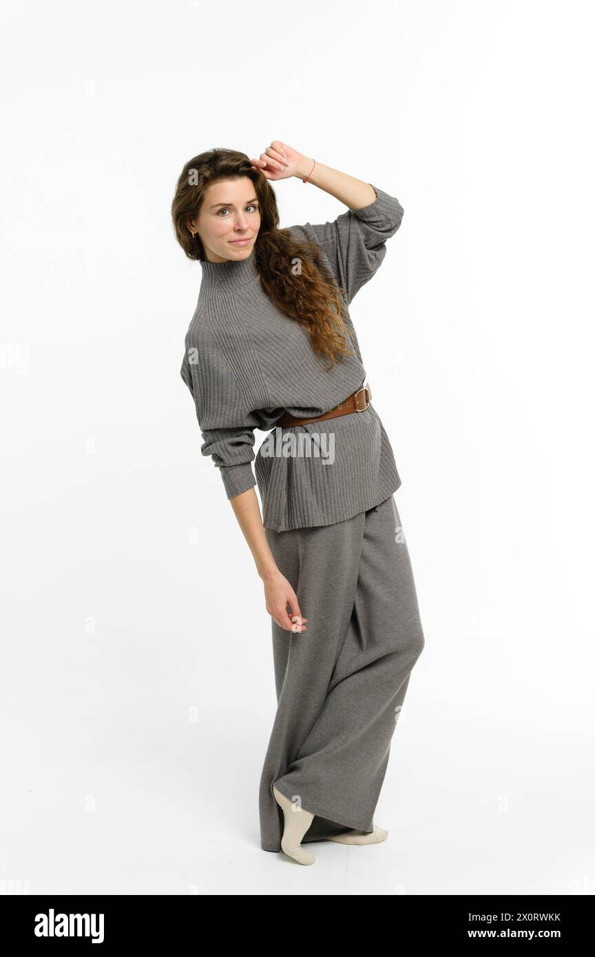 Eine stilvolle Frau trägt einen grauen Pullover und eine Hose mit weitem Bein und zeigt ein modernes modisches Design mit einem einteiligen Kleidungsstück und einer formellen Geste Stockfoto