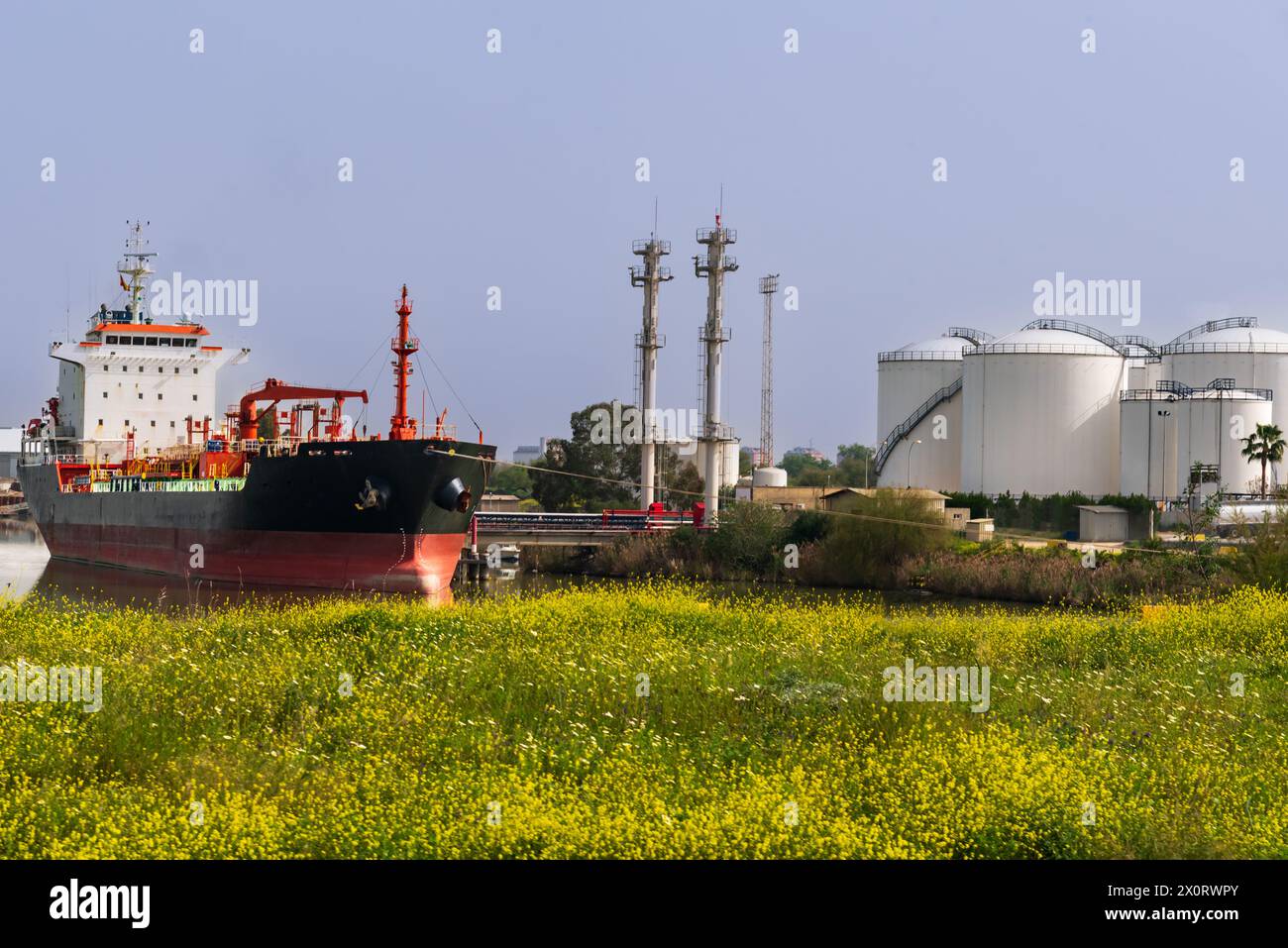 Flüssiges Massenhandelsschiff, das in einem Dock eines Flusshafens neben einigen riesigen Lagerhäusern vor Anker liegt. Stockfoto