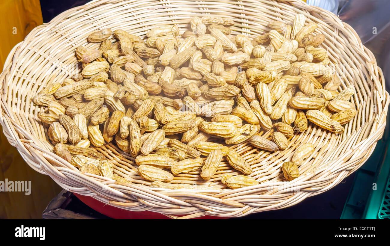 Der Korb aus Korb überfließt goldbraun geröstete Erdnüsse, die einen rauchigen Duft versprühen und gesunde Straßengerichte verkörpern und Nussliebhaber nach sa einladen Stockfoto