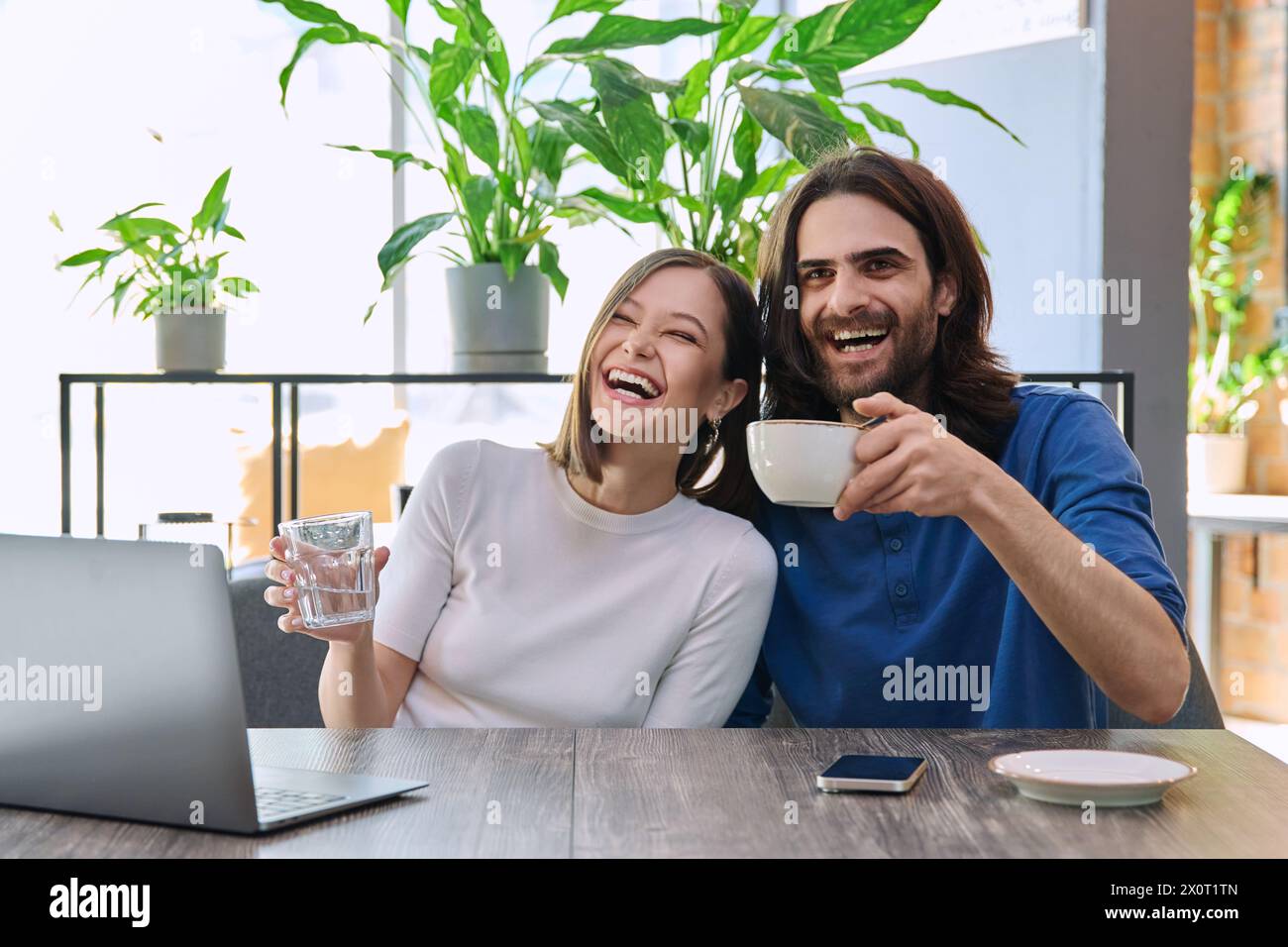 Glückliches lachendes junges Paar, das zusammen in der Cafeteria auf den Laptop blickt Stockfoto