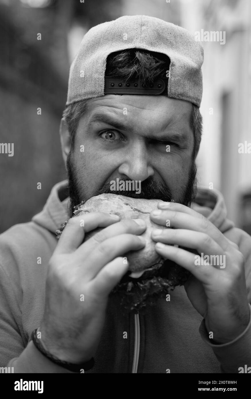 Hunger man isst Burger im Freien. Der Mann isst leckeren Hamburger auf der Straße. Burger zum Mittagessen. Cheeseburger oder Hamburger. Mann isst leckere Burger draußen. Lecker Stockfoto