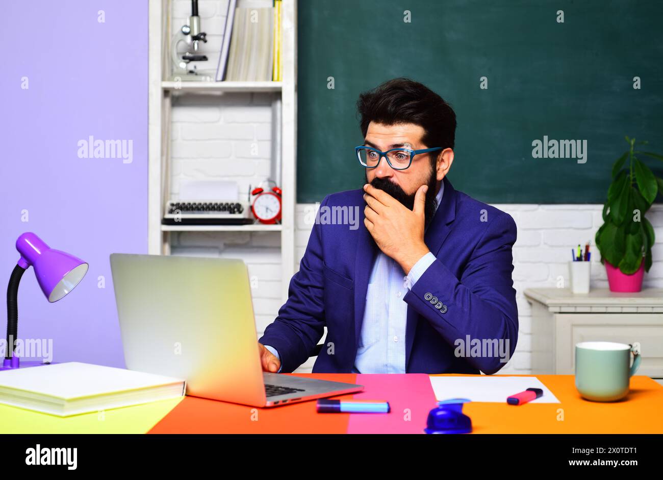 Beruf, Lernen, Bildung und Wissenskonzept. Lehrerjob. Ein überraschter Universitätslehrer arbeitet im Klassenzimmer an einem Laptop. High School Stockfoto